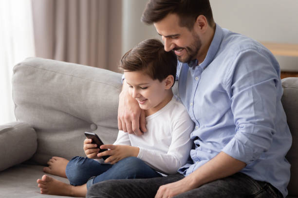 istock Father embrace little son sit together on couch using smartphone 1263052885