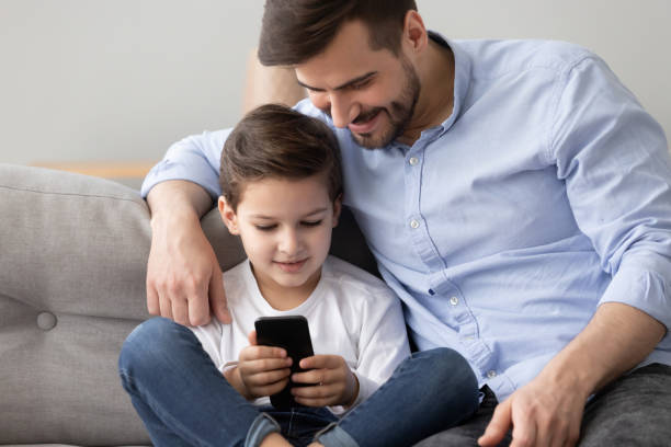 istock Father and little son sitting together on sofa using smartphone 1263052893
