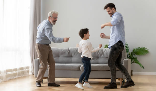 Full-length three generations of men dancing in living room Three generations of active men dancing in living room little boy enjoy time with elderly grandfather and young father, concept of warm relations, understanding, best friends, intergenerational family dancing dad stock pictures, royalty-free photos & images