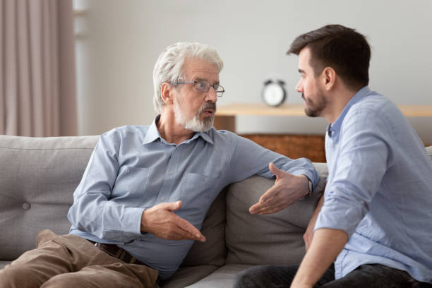 un padre anciano serio y un hijo adulto sentados en el sofá hablando - adult offspring family multi generation family senior adult fotografías e imágenes de stock