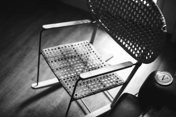An old wooden chair in front of a wall.  The chair is illuminated so that it casts a soft shadow on the wall.