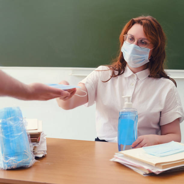 a female teacher gives a medical mask to a student in the hand. training and exams at school in the midst of a coronavirus epidemic - medical student healthcare and medicine book education imagens e fotografias de stock