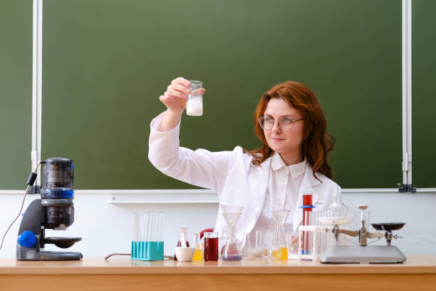 chemistry teacher looks at the reaction of a reagent in a flask. scientific research in a school class in a chemistry lesson - professor scientist chemistry teacher imagens e fotografias de stock