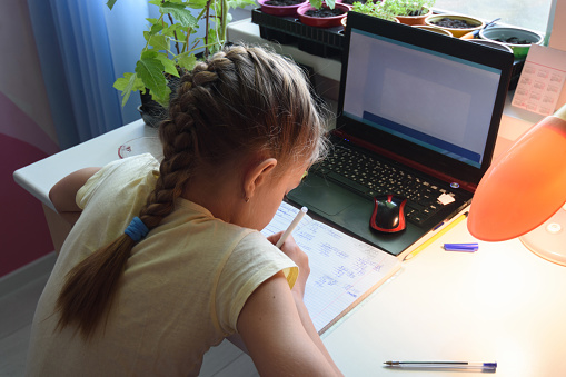 Chica resuelve ejemplos matemáticos en cuaderno frente a portátil photo