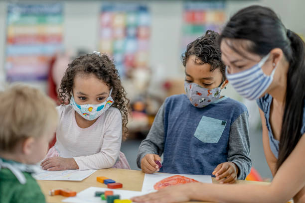 grupo de niños coloreando mientras usa máscaras - preschool teacher fotografías e imágenes de stock