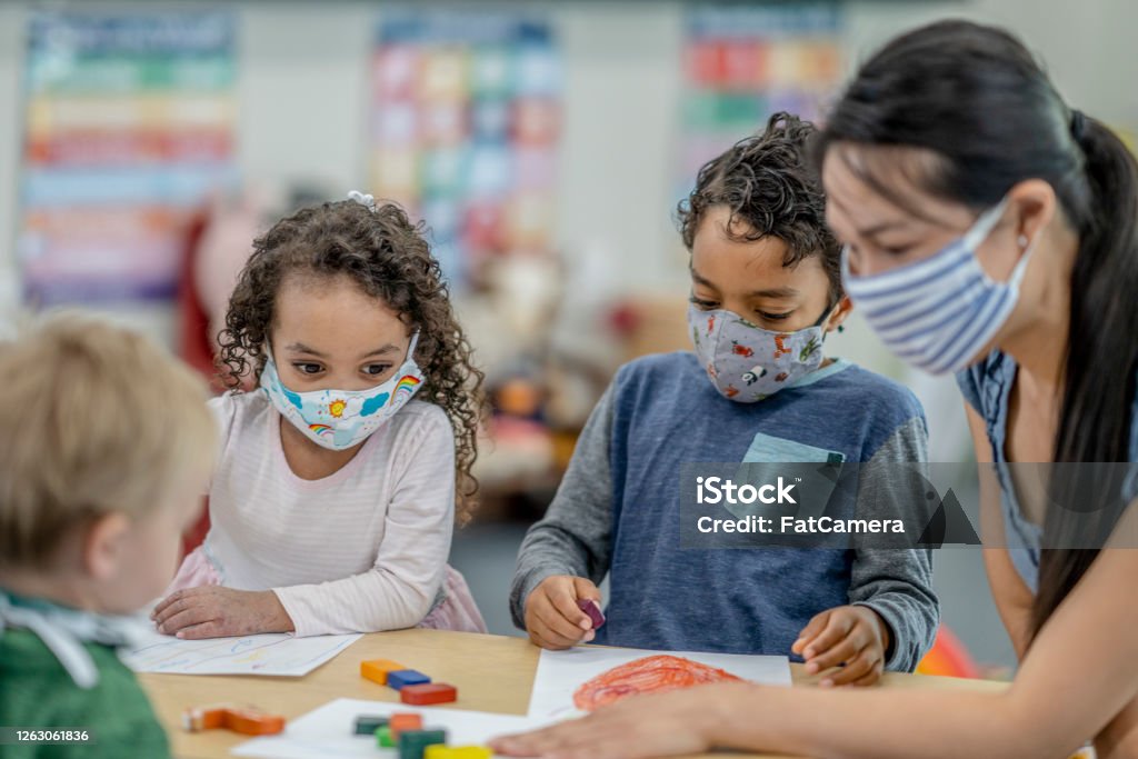 Group of children colouring while wearing masks Multi-ethnic group of children colouring at a table while wearing protective face masks to avoid the transfer of germs. Protective Face Mask Stock Photo