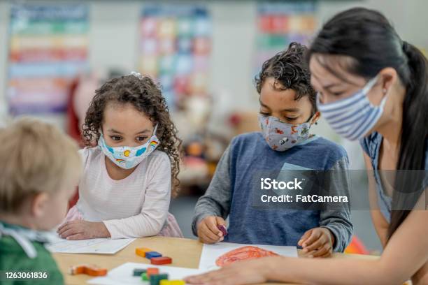 Group Of Children Colouring While Wearing Masks Stock Photo - Download Image Now - Protective Face Mask, Child, Child Care