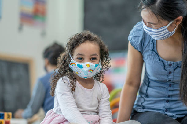 4 year old girl wearing a protective face mask at daycare Young, mixed race girl smiling at the camera while wearing a protective face mask. new normal concept stock pictures, royalty-free photos & images