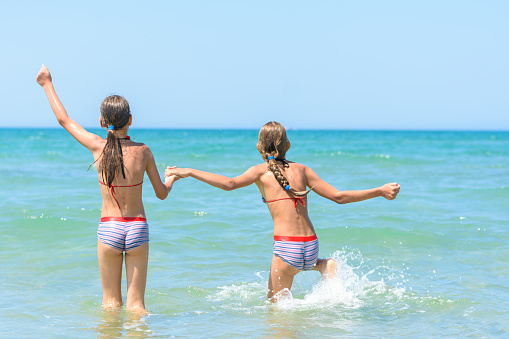 Sisters joyfully and happily run into the sea on a hot sunny day