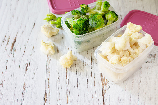 Healthy frozen food for the winter. Containers with frozen cauliflower and broccoli. Copy space.