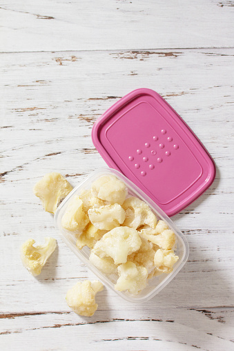 Healthy frozen food for the winter. Containers with frozen cauliflower. Top view flat lay background. Copy space.