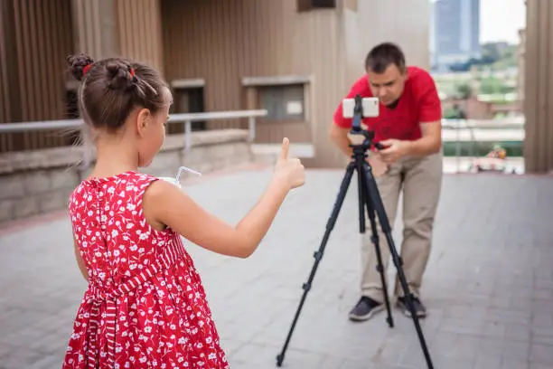 Photo of Make money online. Father recording film with daughter for family channel, video blogger