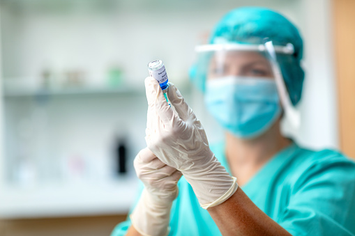 Wearing surgical gloves and mask, filling syringe with COVID-19 vaccine liquid from vial