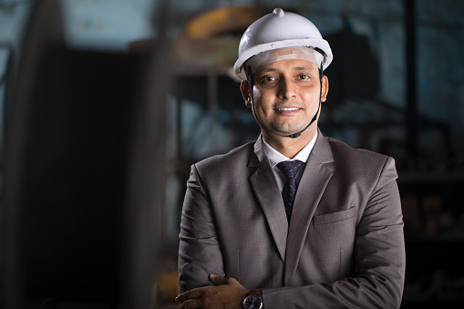 Portrait of confident male engineer with protective hardhat at factory