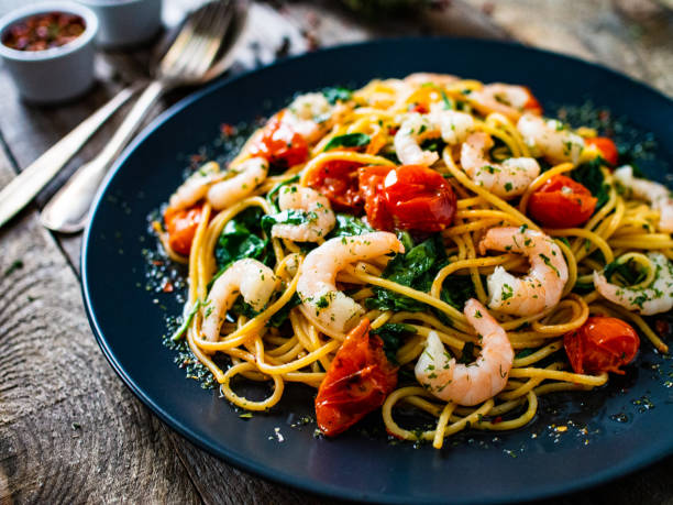 Spaghetti with prawns and vegetables on wooden background stock photo