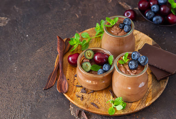 istock Portion jars with chocolate mousse or pudding decorated with sweet cherry, blueberry and mint and pieces of chocolate. Selective focus. Rustic style. Dark background. 1263095695