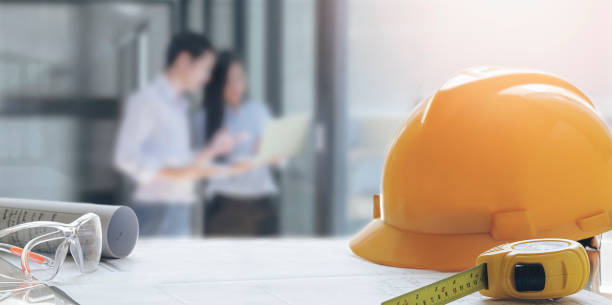 istock Yellow safety  hat and engineering tools on the table with blur image background of engineer team meeting. 1263096110