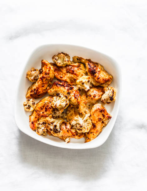 Mustard marinated chicken breast roasted with cauliflower on a light background, top view. Healthy lunch