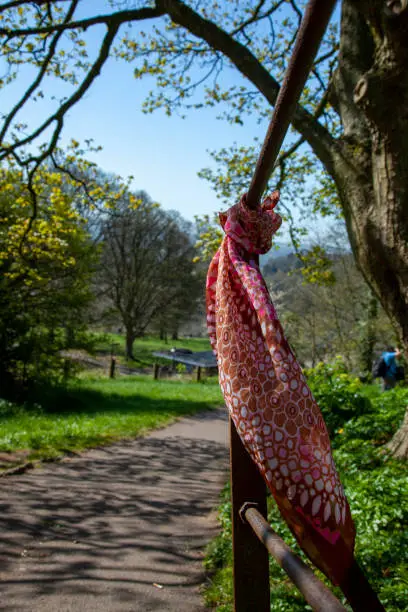 A red scarf is tied to rusted metal railings in a park. It is likely an item that is dropped and then found by someone else or left there as a lucky charm. Scenic view of the park in the background.