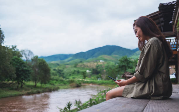 istock a woman using mobile phone while sitting by the river with mountains and nature background 1263100143