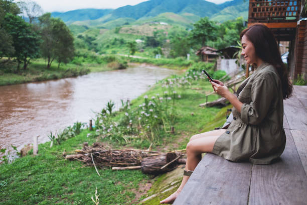 istock a woman using mobile phone while sitting by the river with mountains and nature background 1263100169