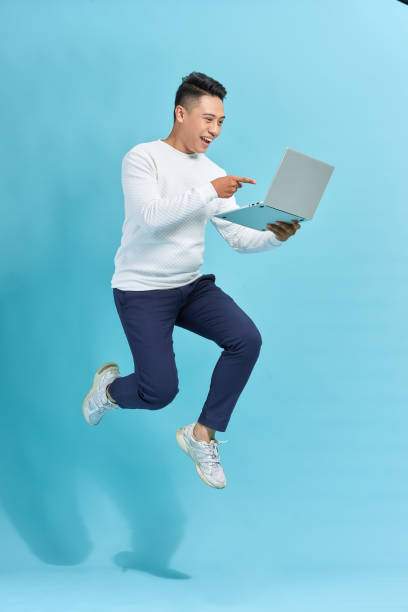 istock Attractive successful guy jumping in air using laptop home-based job isolated over blue background 1263100603