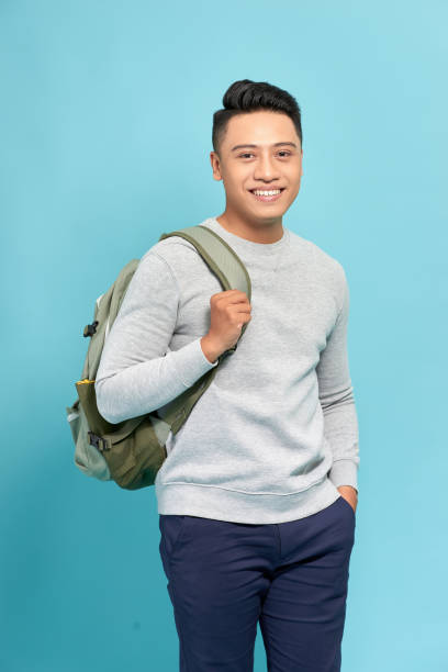 istock Handsome casual guy wearing backpack  laughing and looking away on blue. 1263100756