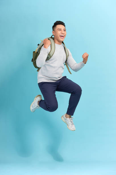 istock Happy young attractive man jumping and waving his hand, wearing in basic clothes with backpack 1263101319