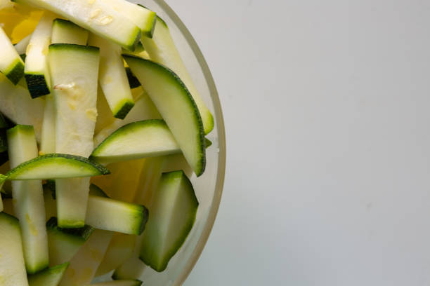 Sliced zucchini slices in a transparent plate on a white background. Raw vegetarian food. Cut the zucchini into small slices. Raw product, green peel.