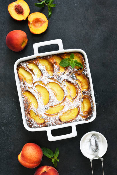 istock Delicate cake with peaches sprinkled with powdered sugar on a black concrete background 1263101499