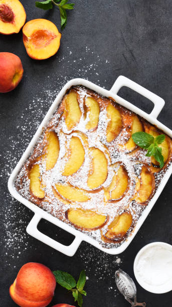 istock Delicate cake with peaches sprinkled with powdered sugar on a black concrete background 1263101538
