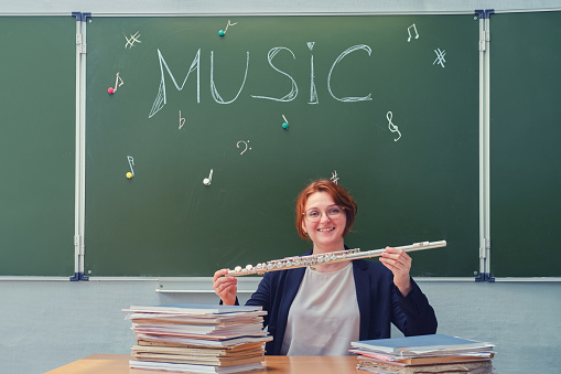 Happy music teacher holds flute in hands in school class