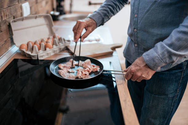 istock Senior man fries bacon in a pan at home. 1263104977
