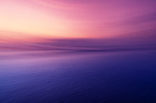 Ocean waves in purple pink sunset, taken with a long exposure.