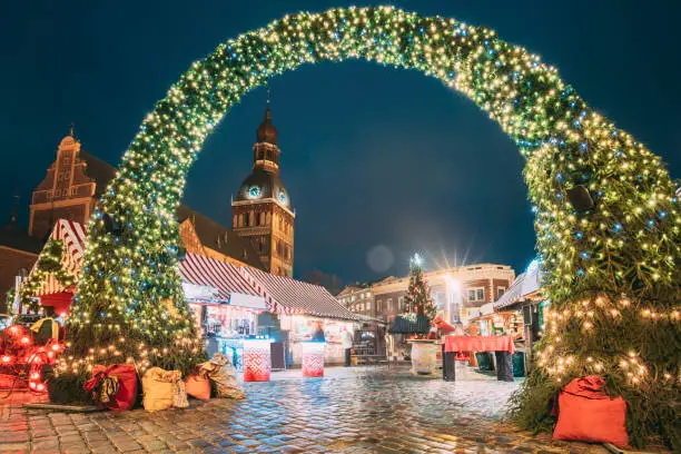 Photo of Riga, Latvia. Xmas Market On Dome Square With Riga Dome Cathedral. Christmas Tree And Trading Houses. Famous Landmark At Winter Evening Night In Illuminations Light