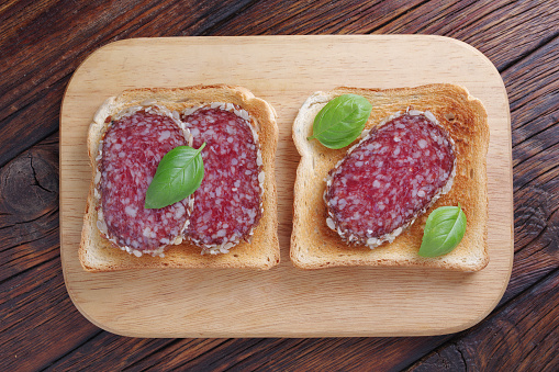 Salami sausage sandwiches on cutting board located on wooden table, top view