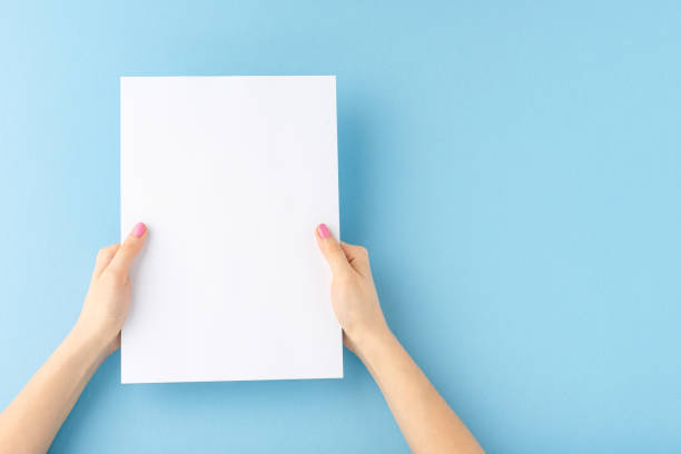 istock Woman’s hands showing white paper with copyspace on blue background. Close up 1263109660