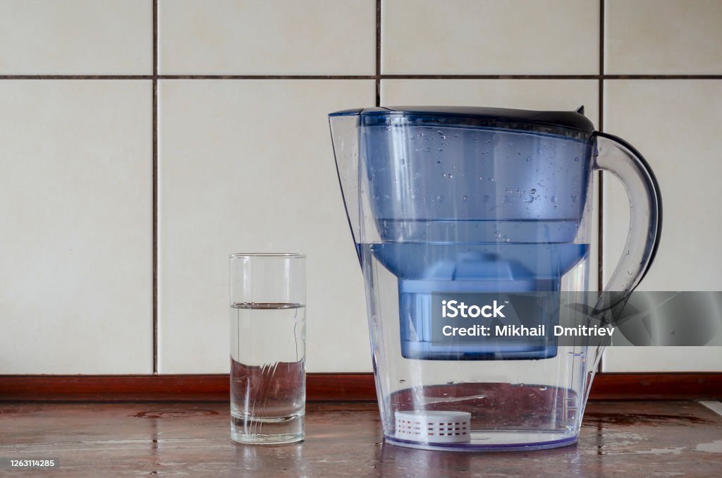 Water filter jug âââwith silicon cartridge inside on the kitchen counter. Water filter jug ââwith silicon cartridge inside on the kitchen counter. Silicon cartridge for saturation of liquid with minerals. Plastic jug and  glass of purified water. Drink water. Water Filter Jug Stock Photo