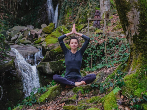 istock Young slim woman practicing yoga outdoors in moss forest on background of waterfall. Unity with nature concept. Girl meditates sitting 1263114416