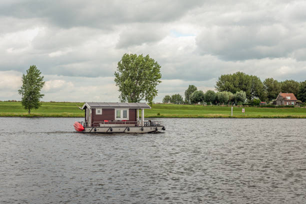 Electric powered log cabin boat with solar panels sailing on a Dutch river. It is a cloudy day in the summer season.
