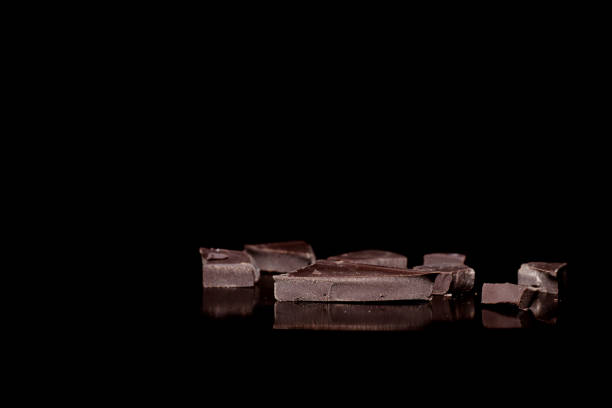 Close-up pieces of black bitter chocolate lying on a mirror surface isolated on black background, low key.