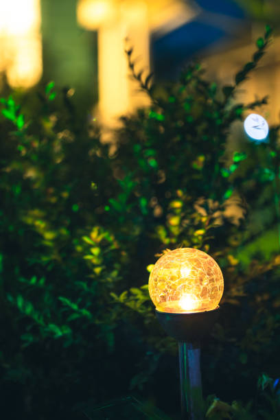 istock Night View Of Flowerbed Illuminated By Energy-Saving Solar Powered Colorful Multi-colored Lantern On Yard. Beautiful Small Garden With Yellow Light, Lamp In Flower Bed. Garden Design 1263121380