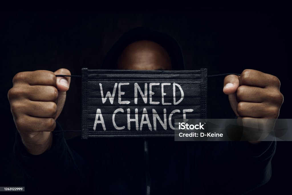Stop racism Afroamerican man wearing hoodie holds black facial mask with inscription We Need A Change. Anti-racism concept. Anti-racism Stock Photo
