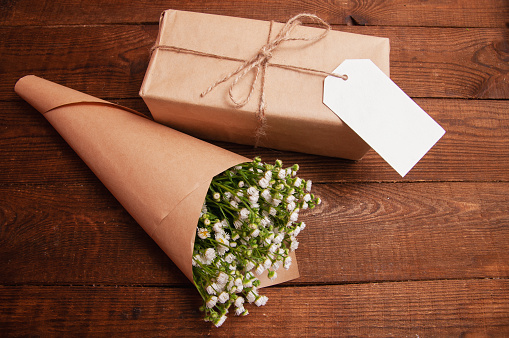 gift is wrapped in craft paper, next to it is a bouquet of chamomile flowers lying on a wooden table