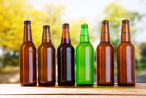 coloured beer bottles on table on blurred forrest background, holiday concept