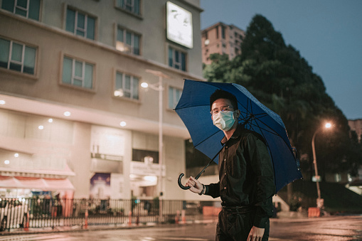 an asian chinesee teenage boy holding umbrella walking in the rain at night in a busy street