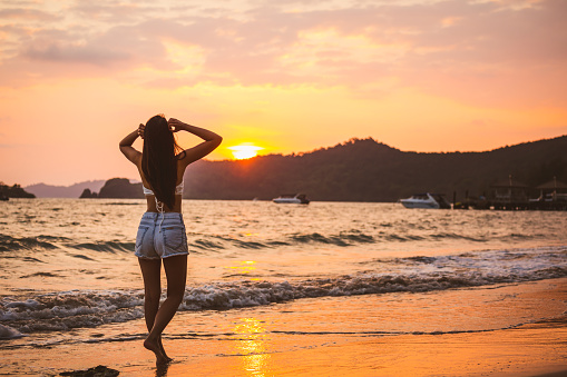 Summer travel vacation concept, Traveler asian woman with bikini relax on beach at sunset in Koh Mak, Thailand