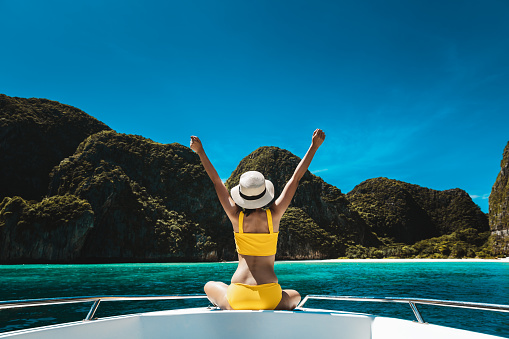 Travel summer vacation concept, Happy solo traveler asian woman with bikini and hat relax on boat in Maya Bay Phuket Thailand