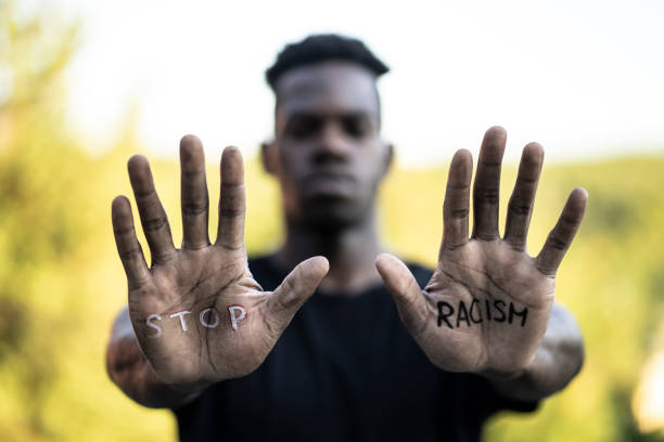 "Stop Racism" message concept African-American man standing outdoors and looking at the camera. He's showing a message that says "Stop Racism" on his hands. affirmative action photos stock pictures, royalty-free photos & images