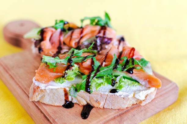 Sandwich with red fish,  cheese and arugula on a board.  Selective soft focus. Copy space